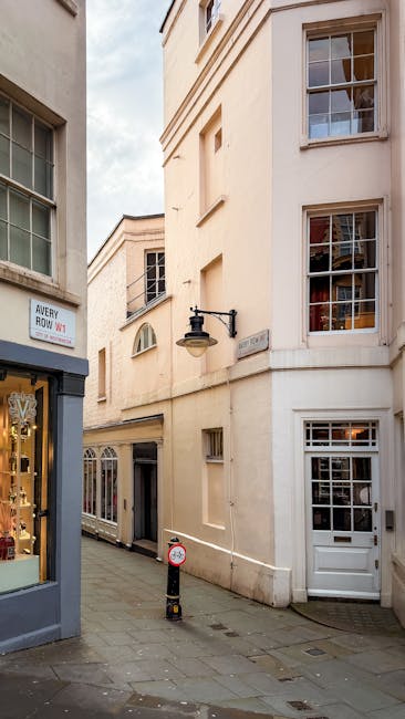 The image shows a city street scene in Mayfair during daylight hours, with several multi-storey buildings featuring large windows and a mix of modern and classic architecture. In the foreground, a bla